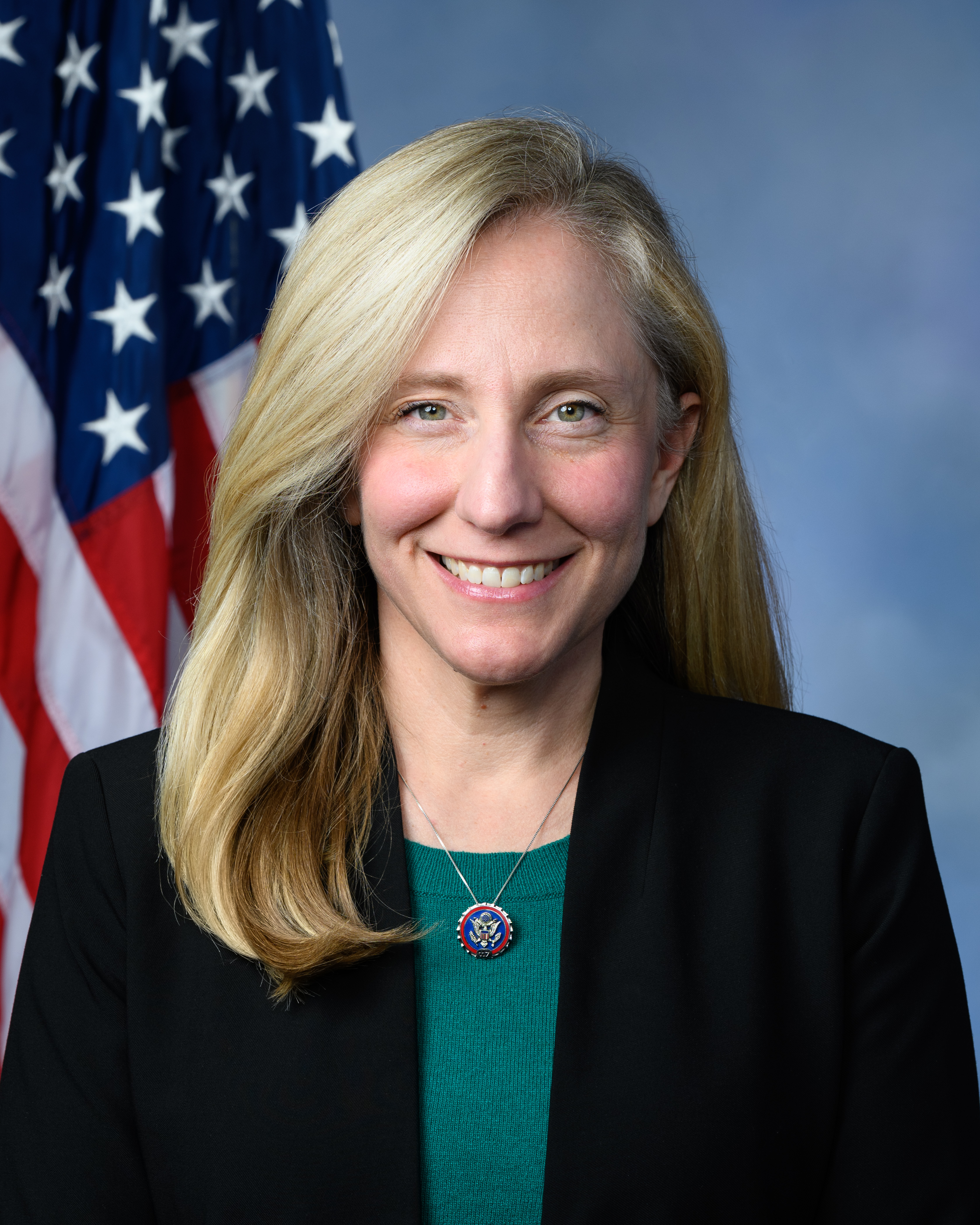 Abigail Spanberger smiling in her official House portrait, US flag behind her and a Great Seal medallion at the collar of a green sweater, 2019