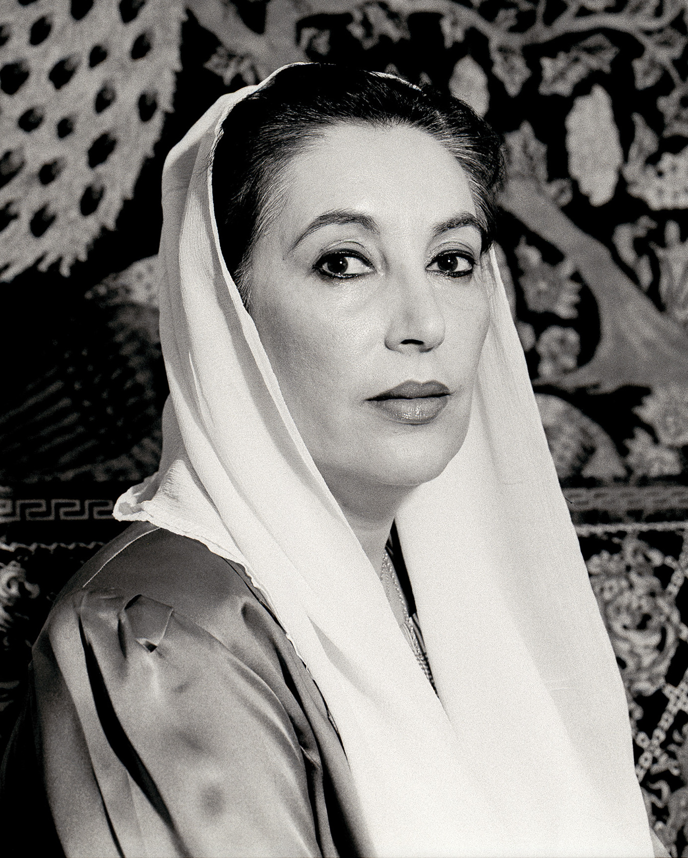 Benazir Bhutto in a black-and-white portrait in a white dupatta against an embroidered backdrop, 2007