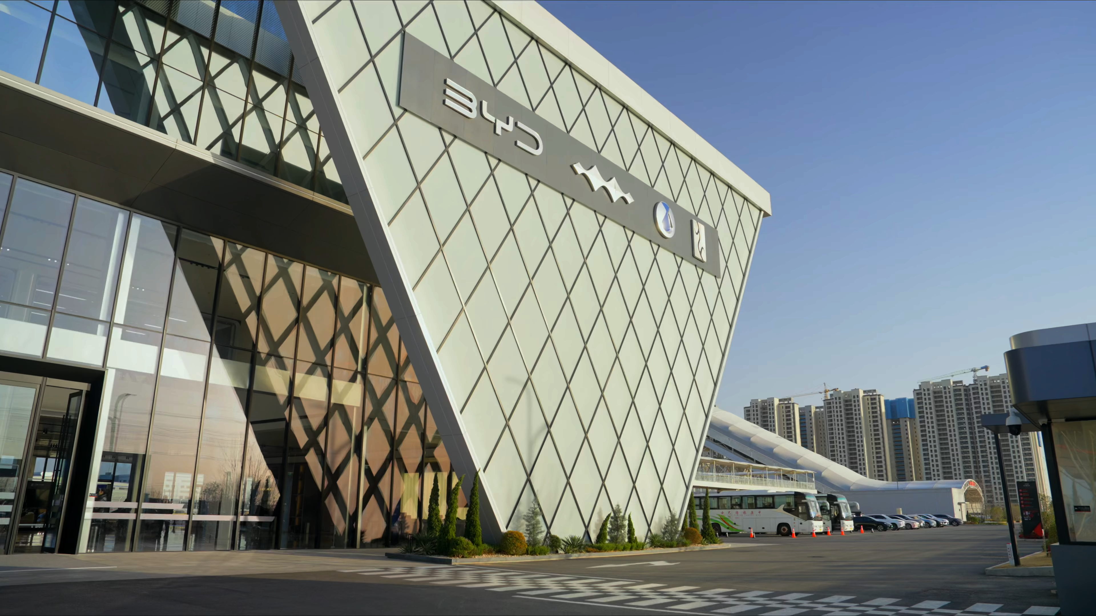 The angular glass entrance of the BYD experience center, silver BYD lettering on a diamond-panelled canopy above the car-park drive, 2023