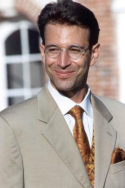 Daniel Pearl smiling in a tan suit and gold paisley tie against a red-brick European facade, 2000