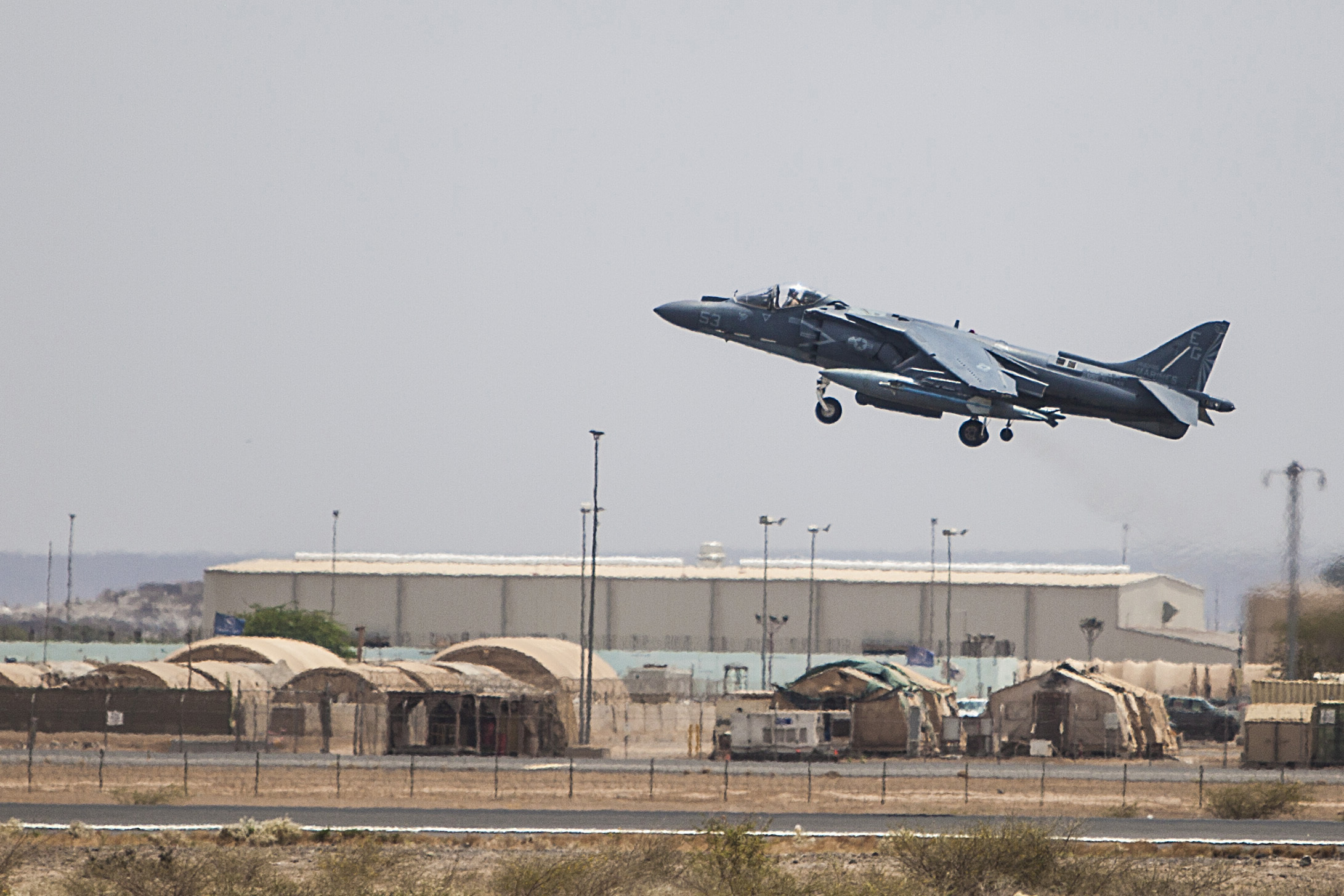 A US Marine AV-8B Harrier lifting off the runway at Camp Lemonnier in Djibouti, hangars and canvas tents in the background, 2015
