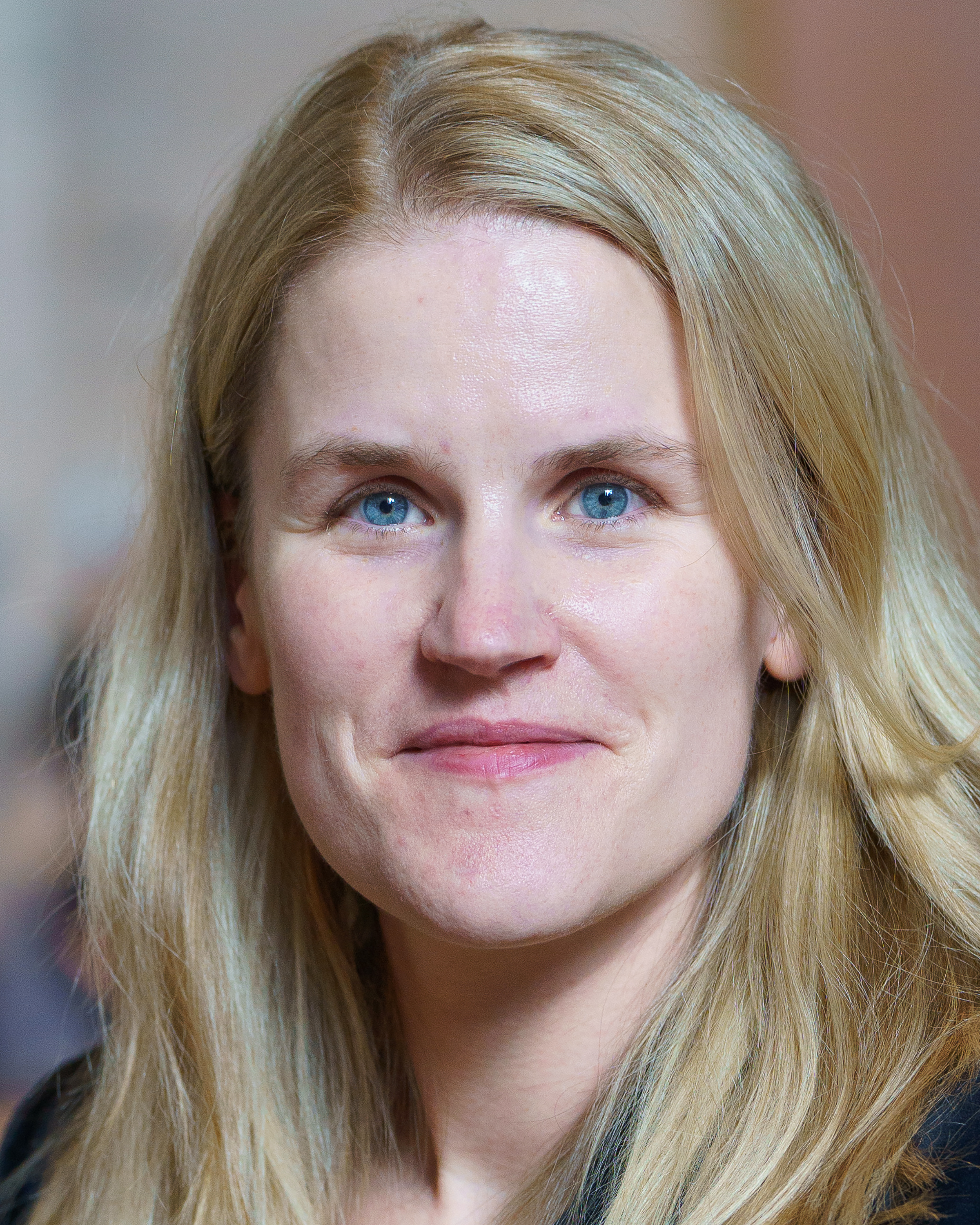 Frances Haugen in a candid portrait, blonde hair falling on both sides of her face against a warm out-of-focus background, 2021