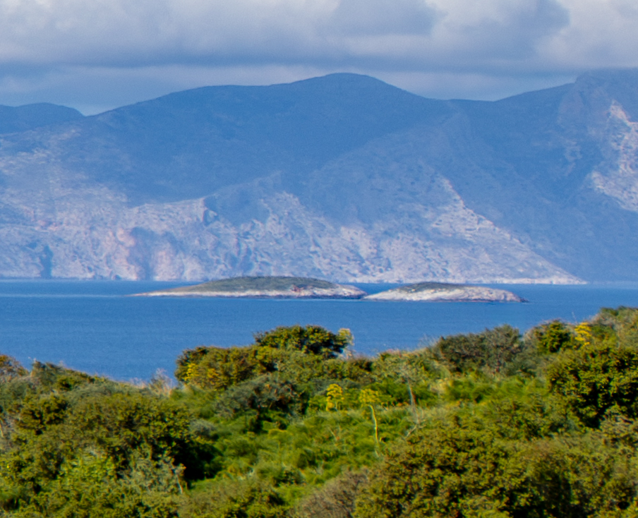 The two low rocky Imia islets in the eastern Aegean, blue sea between them with the Turkish coast rising in the distance, 2015