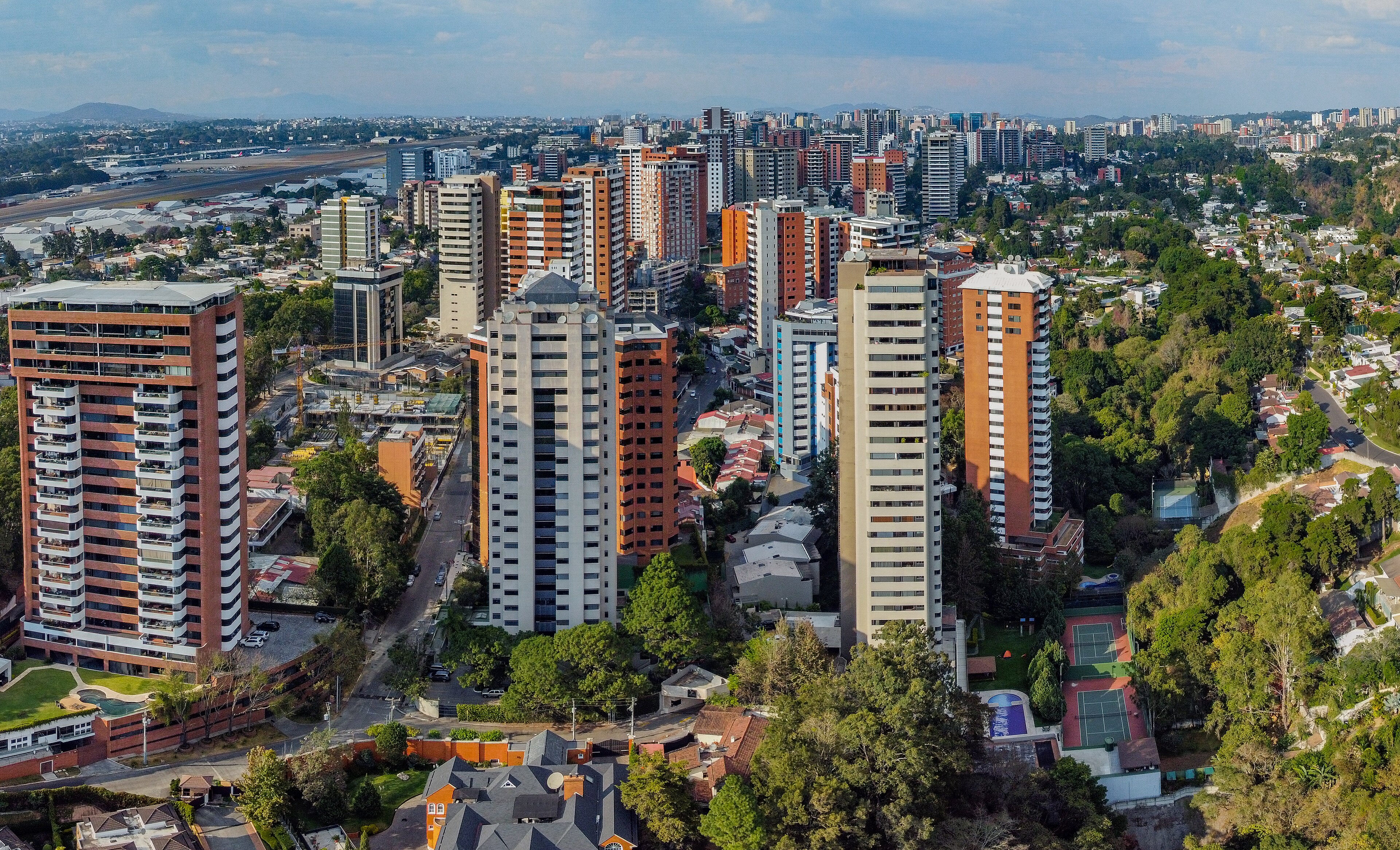 Aerial view of the high-rise district of Guatemala City, apartment towers rising from wooded ridges above the sprawl, 2020