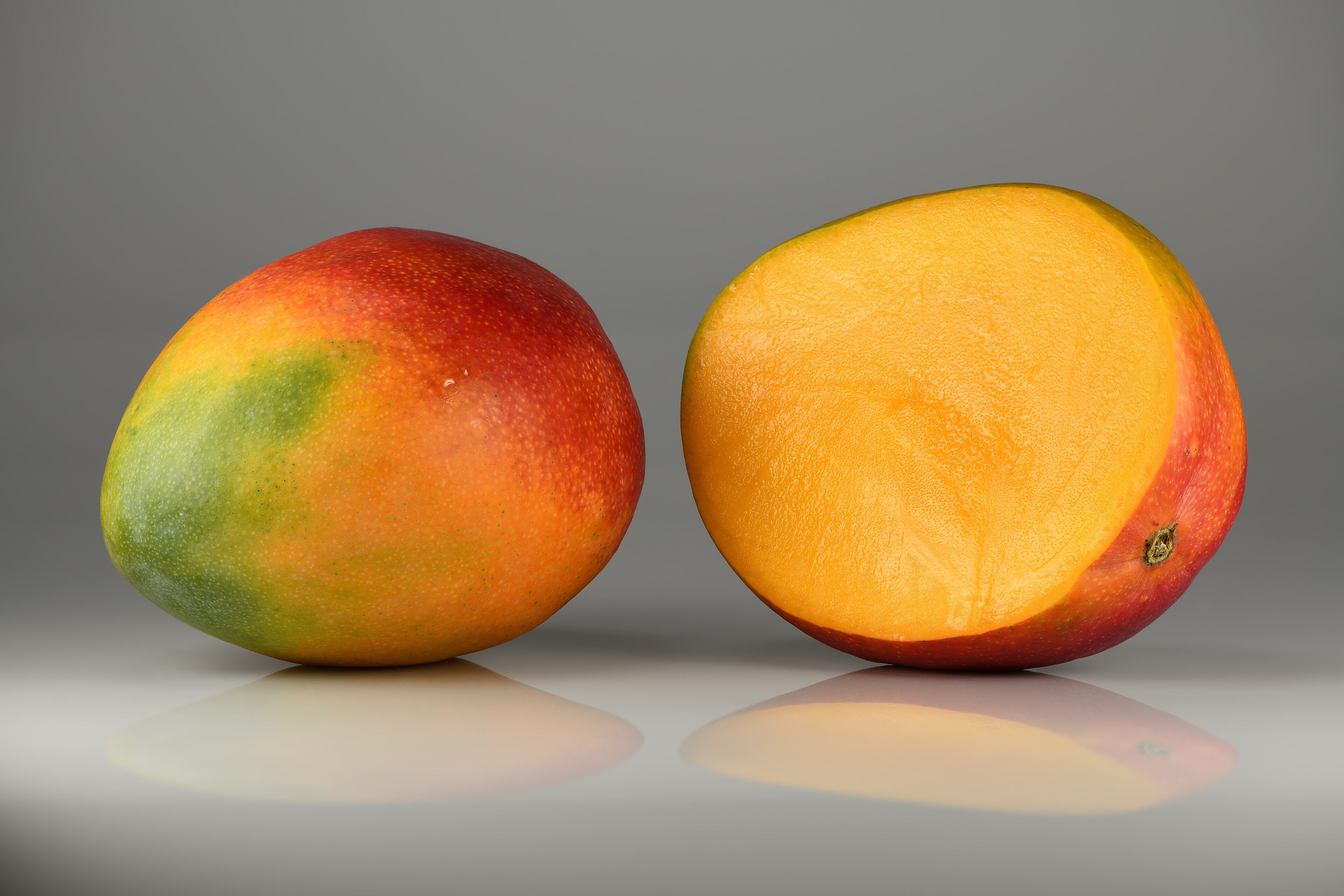 Two ripe mangoes on a grey background, one whole and one halved to show the golden flesh around the pit, 2015