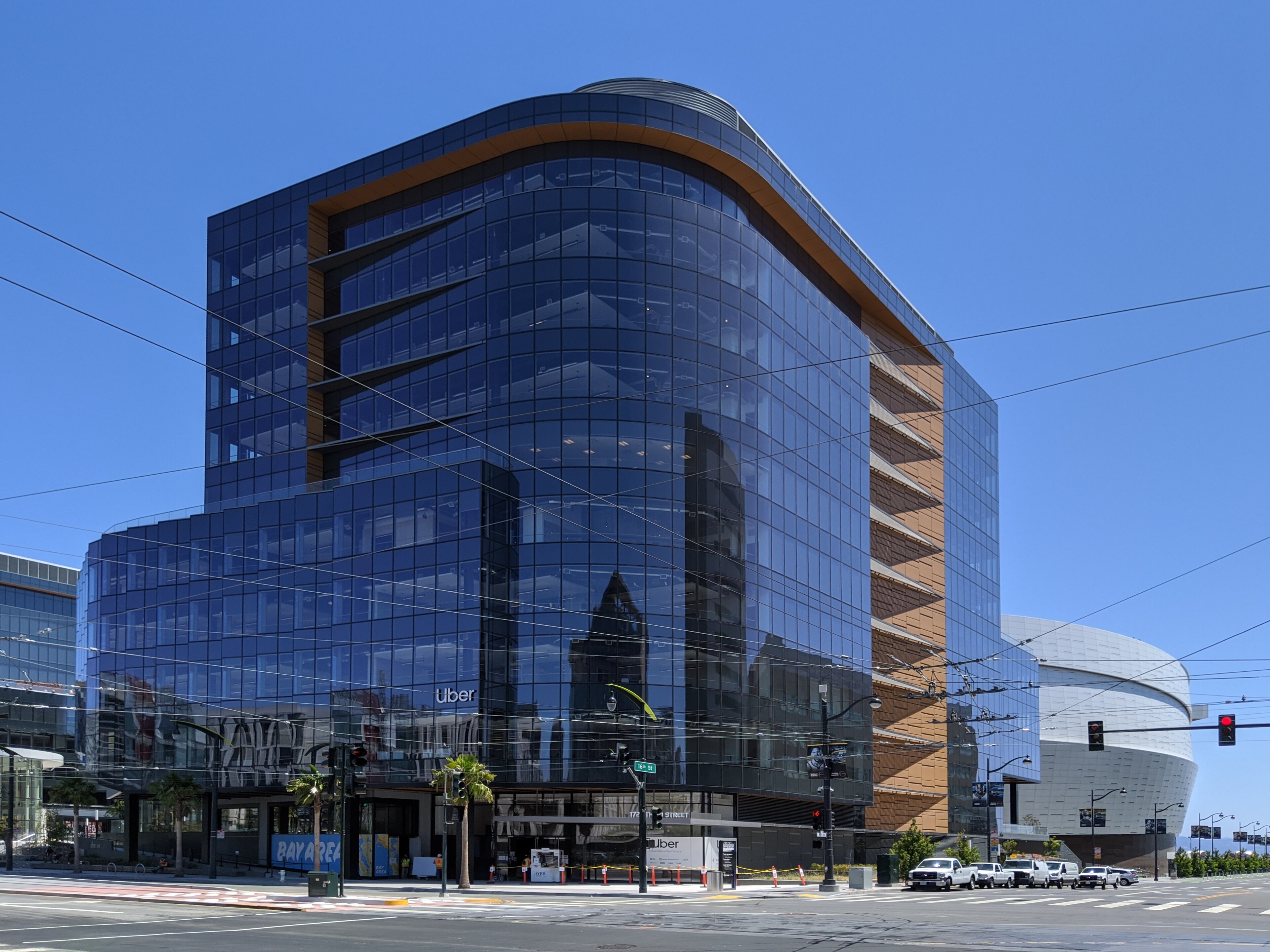 The curved blue-glass Uber headquarters at 1725 16th Street in San Francisco, streetcar wires strung across the intersection, 2020