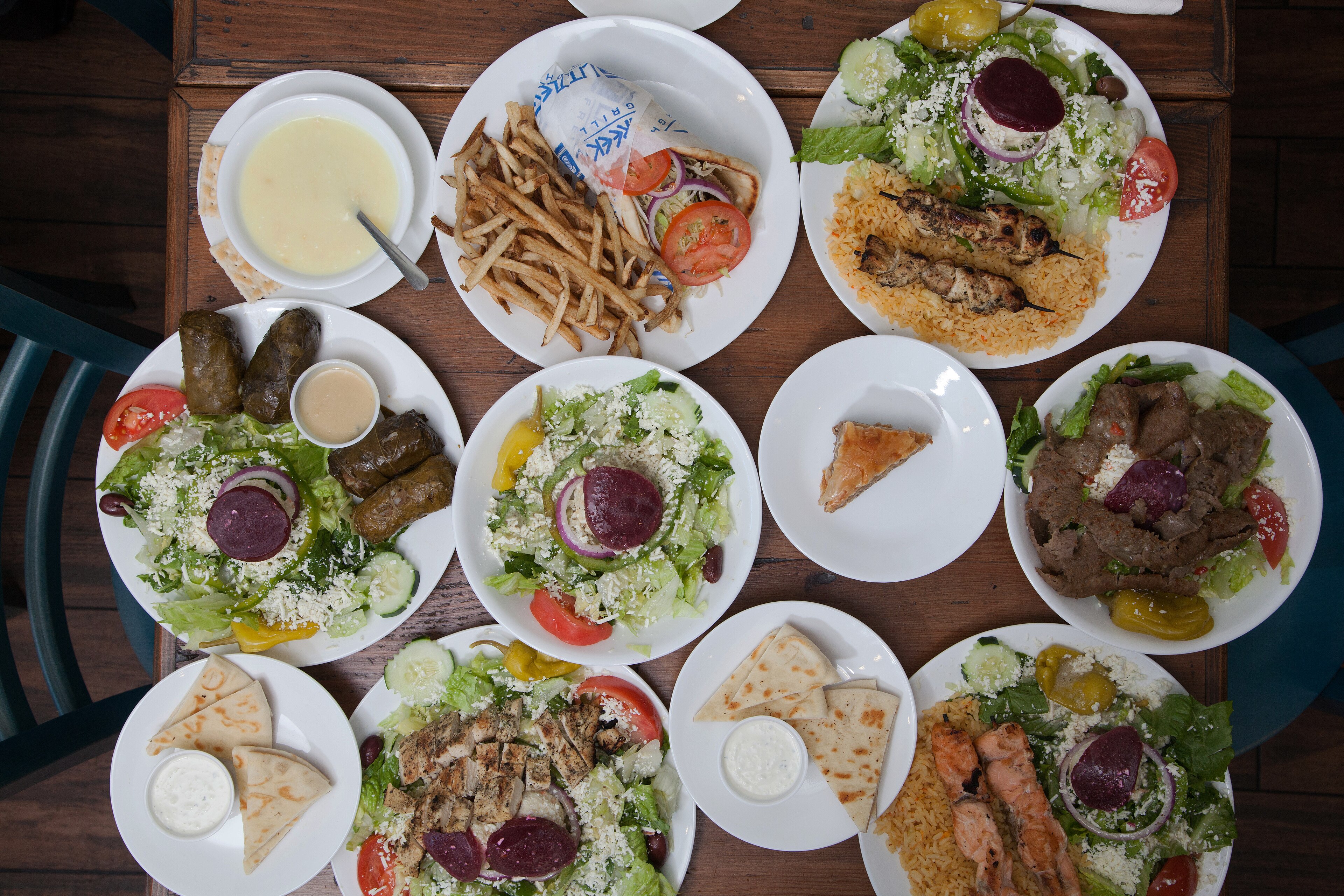 An overhead spread of Greek plates on a wooden table, souvlaki over rice, gyro, salads with feta and dolmades, 2015