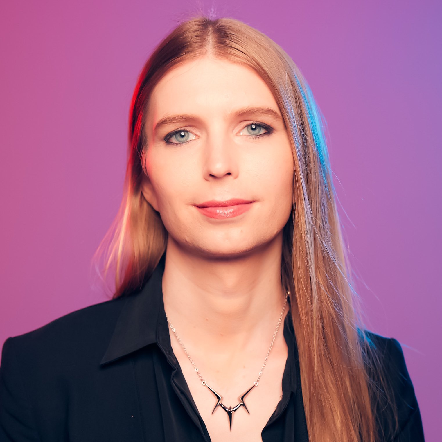 Chelsea Manning in a studio portrait against a magenta backdrop, silver spine necklace over a black blazer, 2017