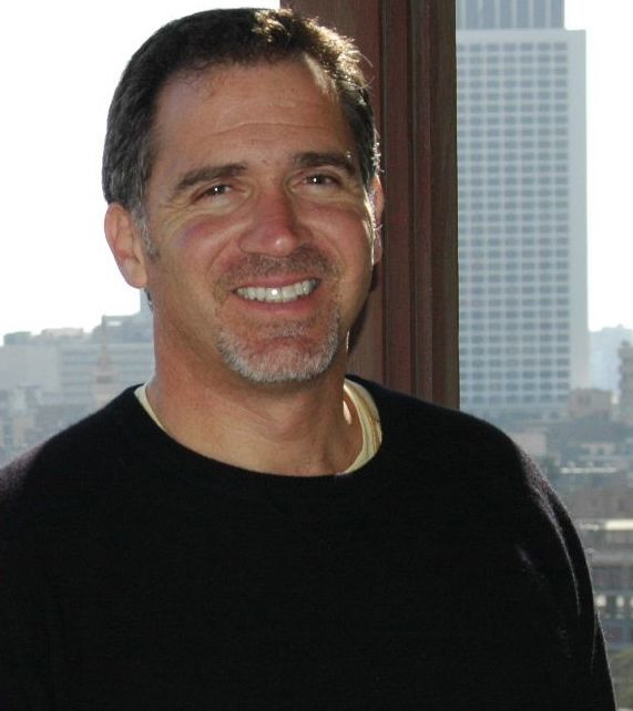 Miko Peled smiling in a dark sweater in front of a downtown Los Angeles window, 2015