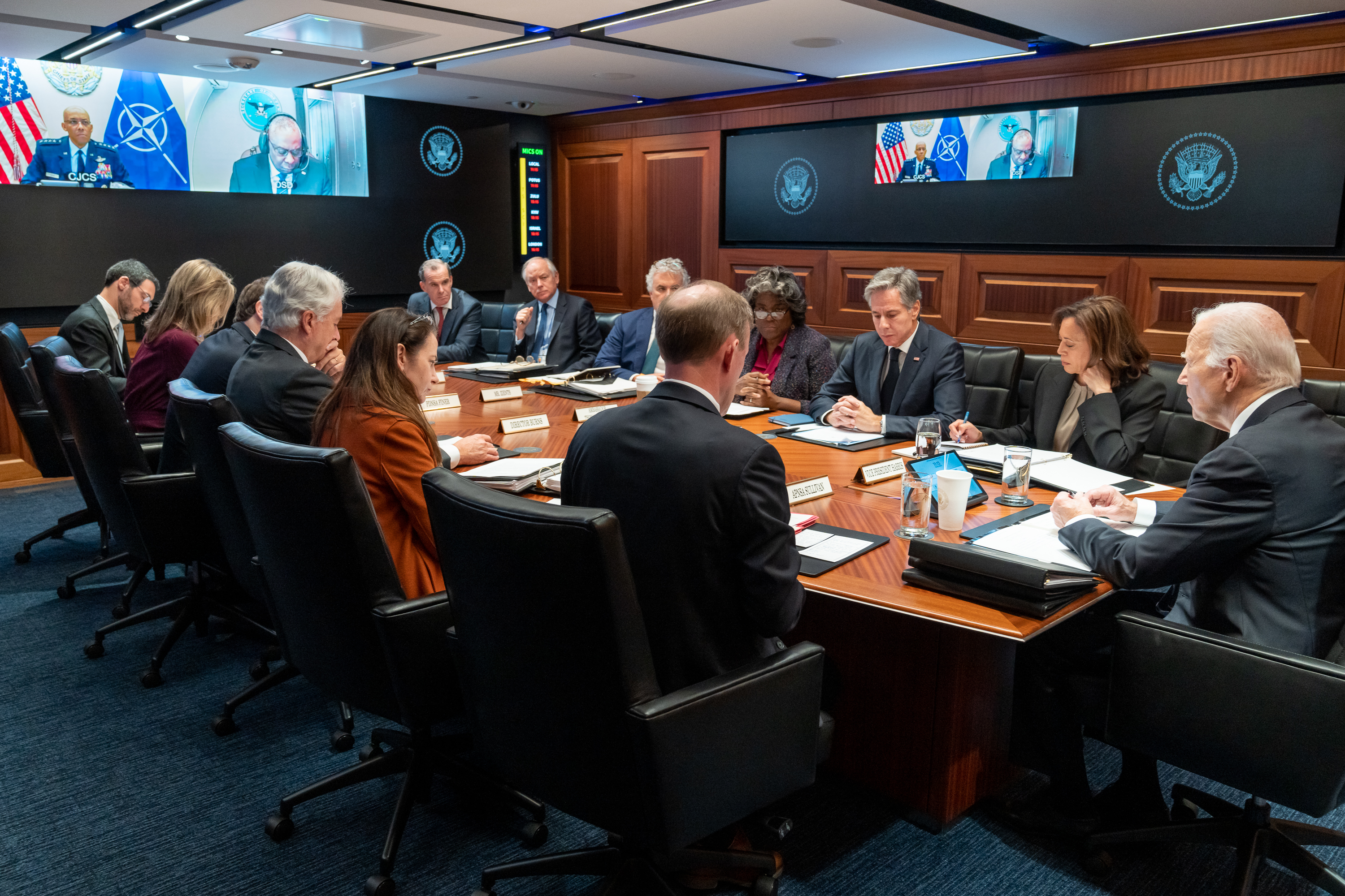 Joe Biden across the Situation Room table from Kamala Harris, Antony Blinken and Linda Thomas-Greenfield during a NATO video call, presidential seals lining the wood-panelled wall, 2023