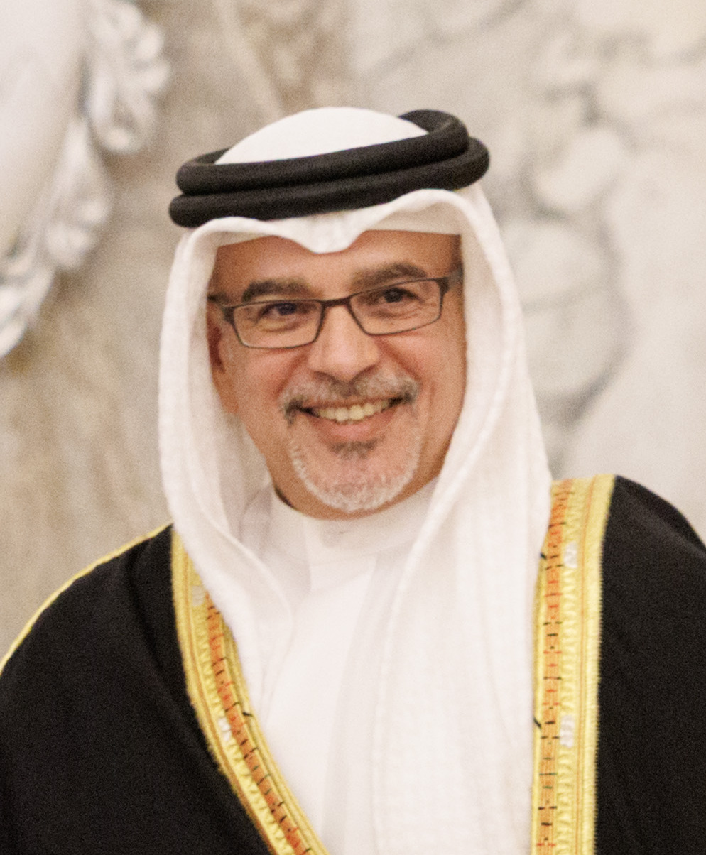 Salman bin Hamad smiling in a white ghutra and black agal, rimless glasses above a gold-trimmed black bisht over a white thobe, 2018