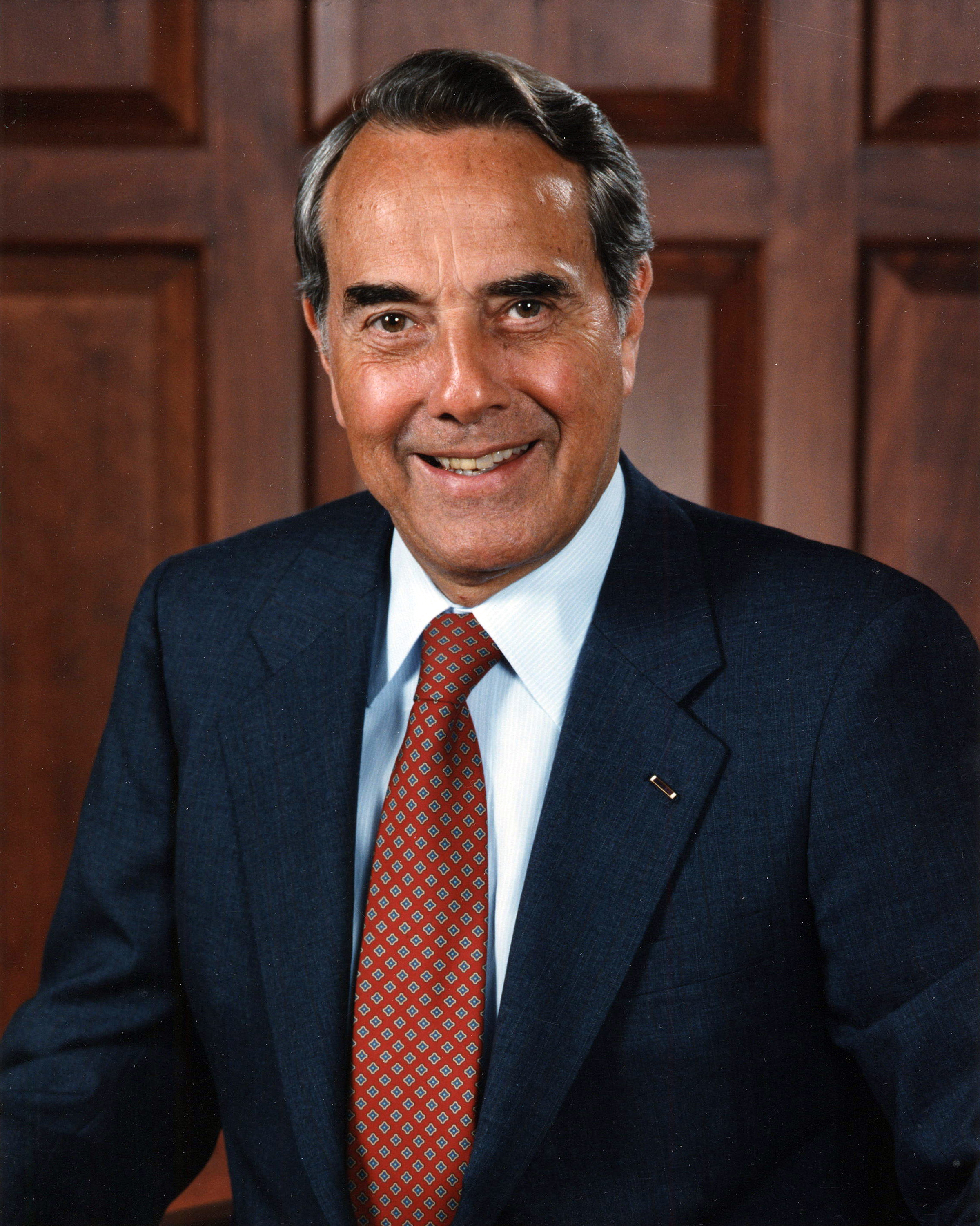 Bob Dole in an official portrait, dark suit over a red-and-blue diamond tie against a wood-panelled wall, 1996