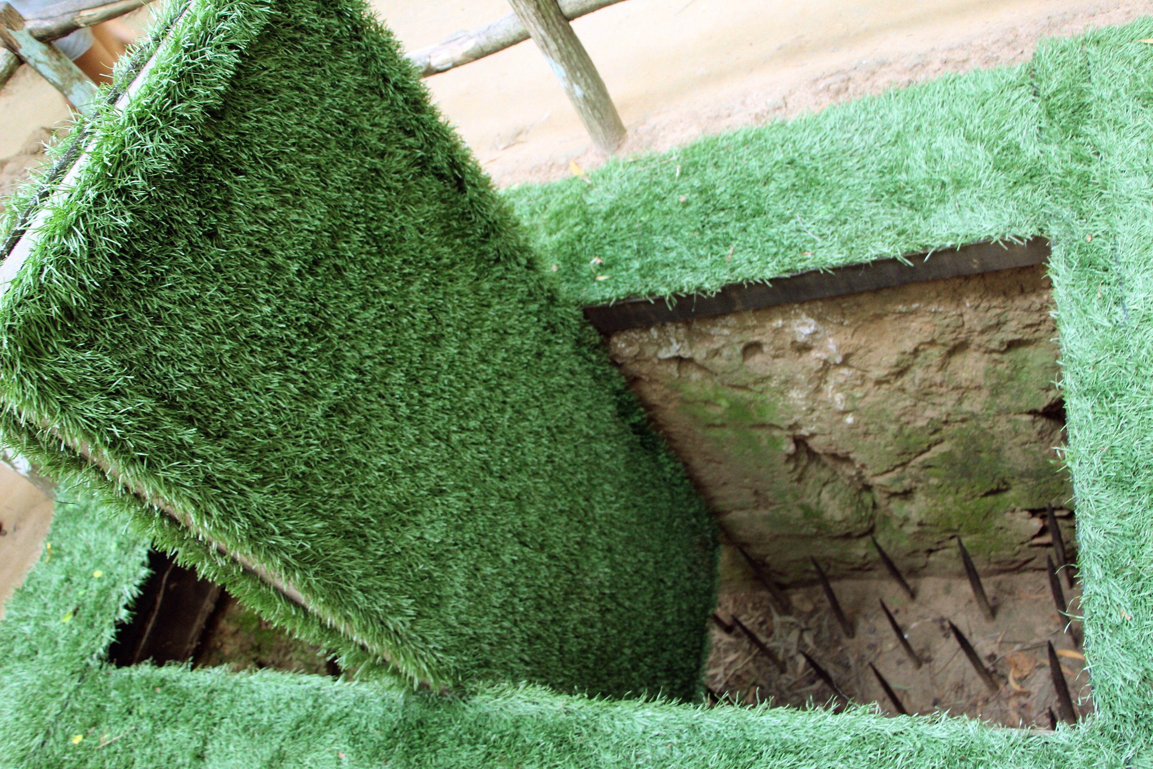 A Vietnamese jungle trapdoor faced with turf lifted to reveal a pit lined with sharpened bamboo spikes at Cu Chi, 2015