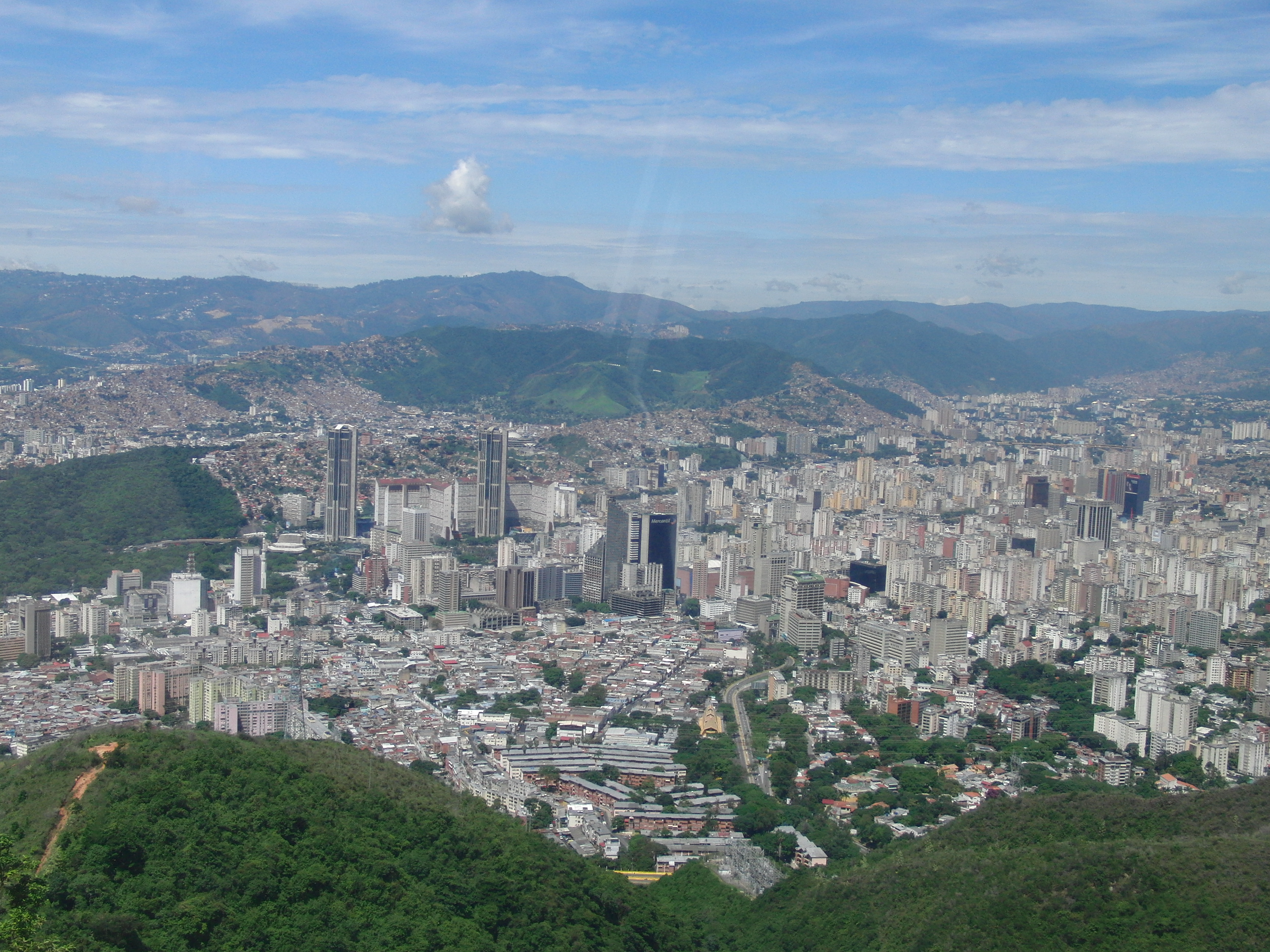 The Caracas skyline from the Ávila mountain, twin towers of Parque Central rising above the sprawl with green ridges receding toward the far cordillera, 2015
