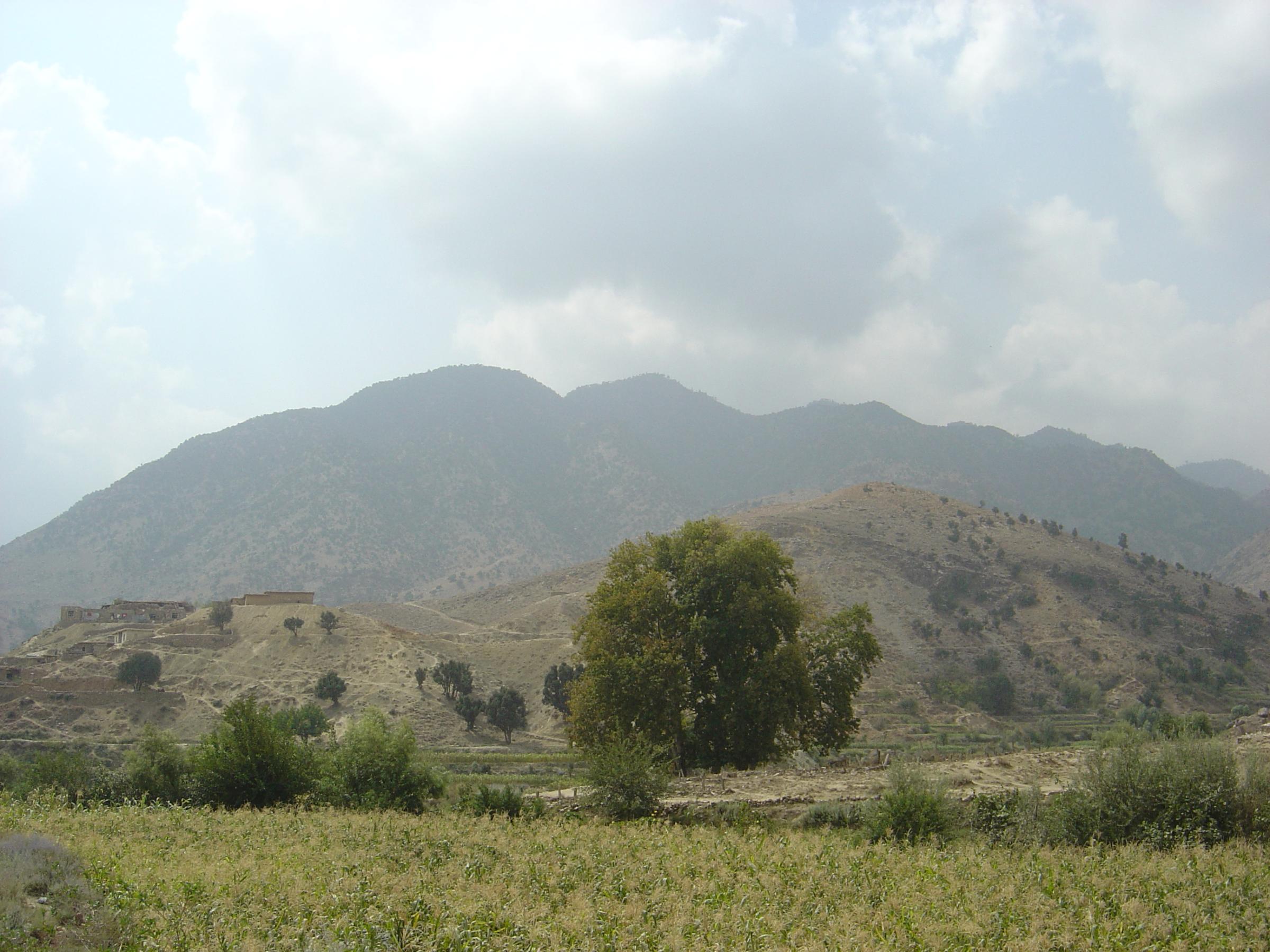 The Tora Bora mountains in eastern Afghanistan, dry ridges above a mud-brick hilltop village and green cornfields in the foreground, 2010