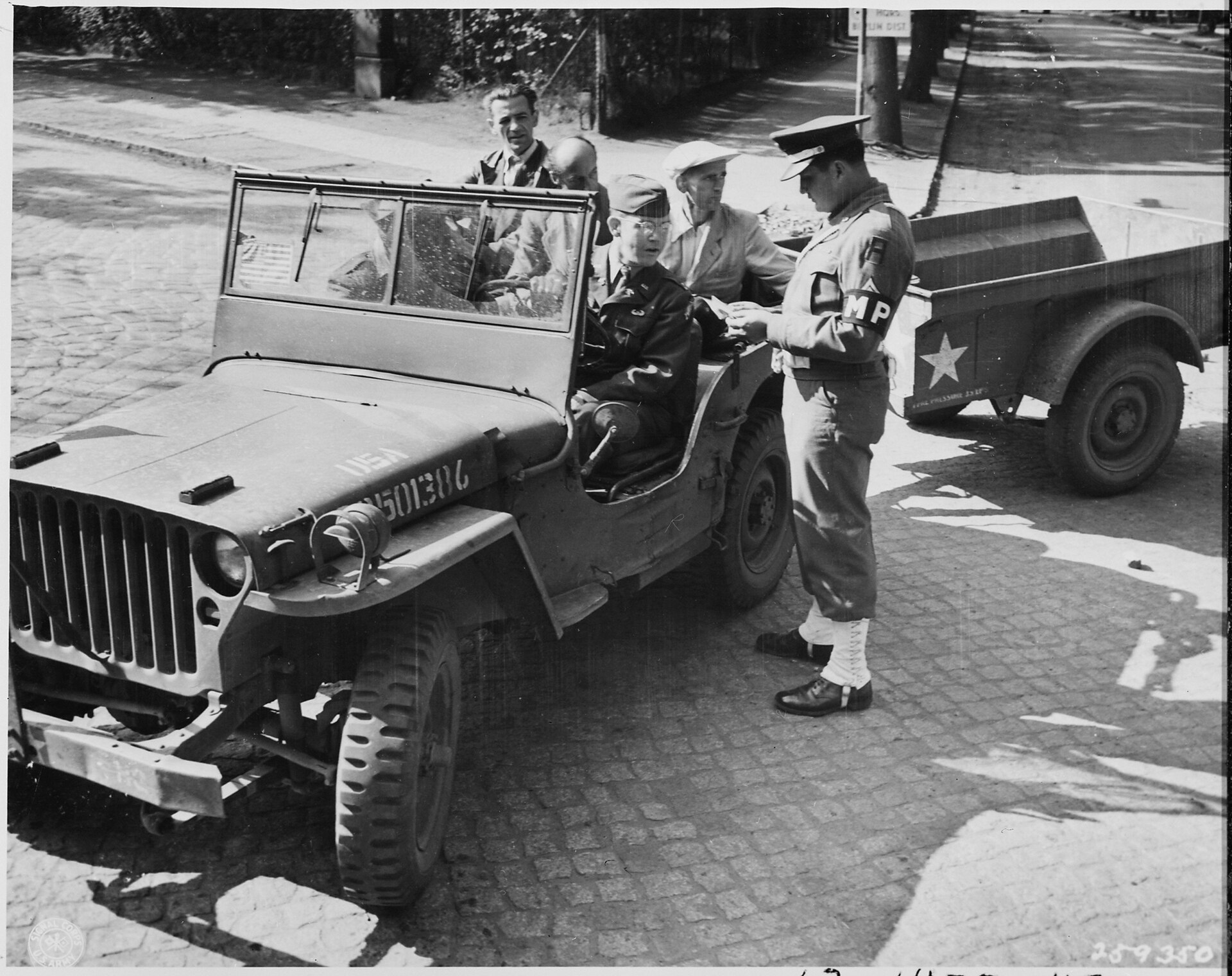 A black-and-white photograph of a US military policeman checking the papers of civilians in a jeep at a Berlin sector checkpoint, 1946