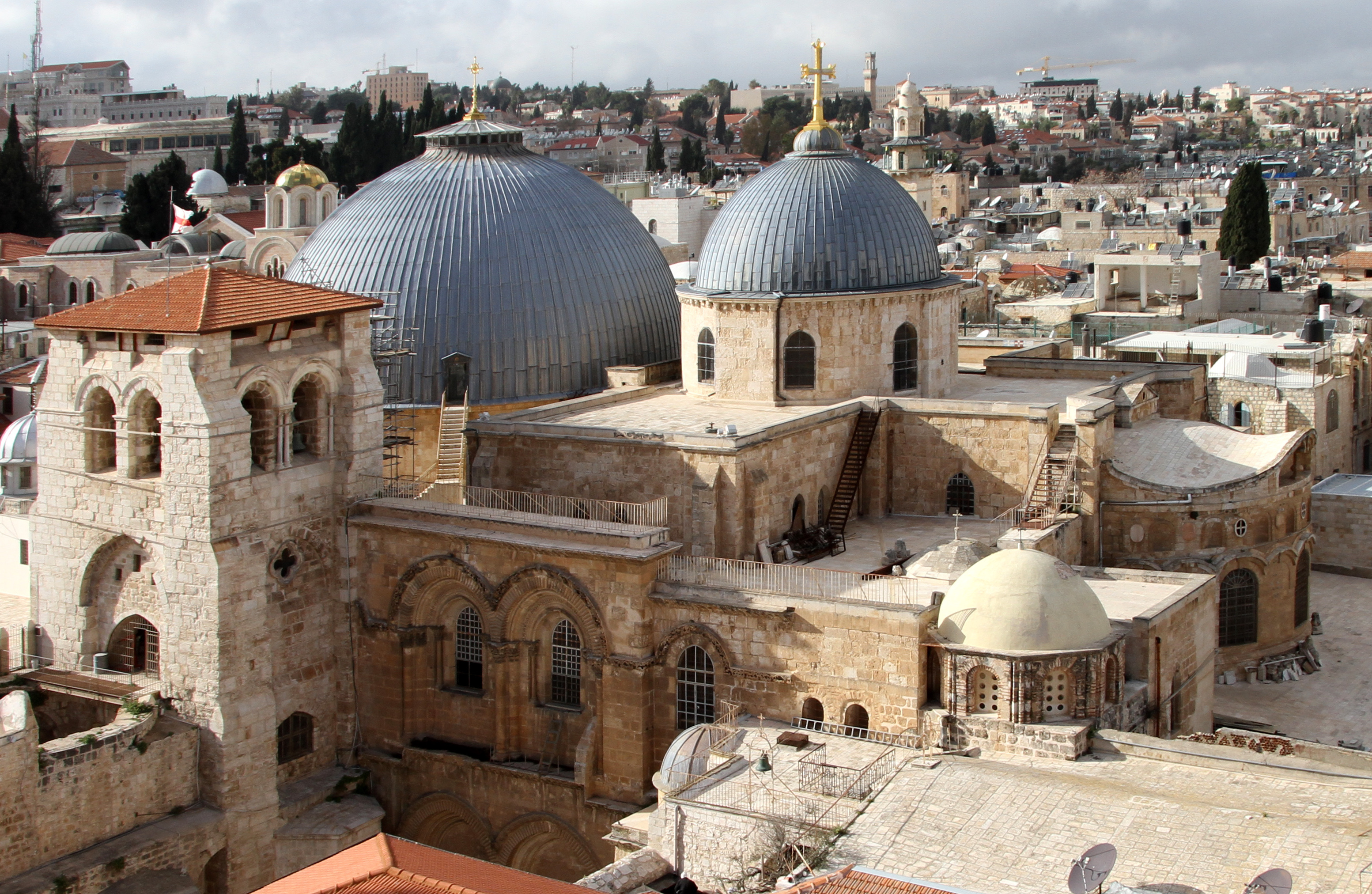 The twin lead domes of the Church of the Holy Sepulchre rising above the tiled roofs of Jerusalem's Old City, cypress trees and the modern city behind, 2015