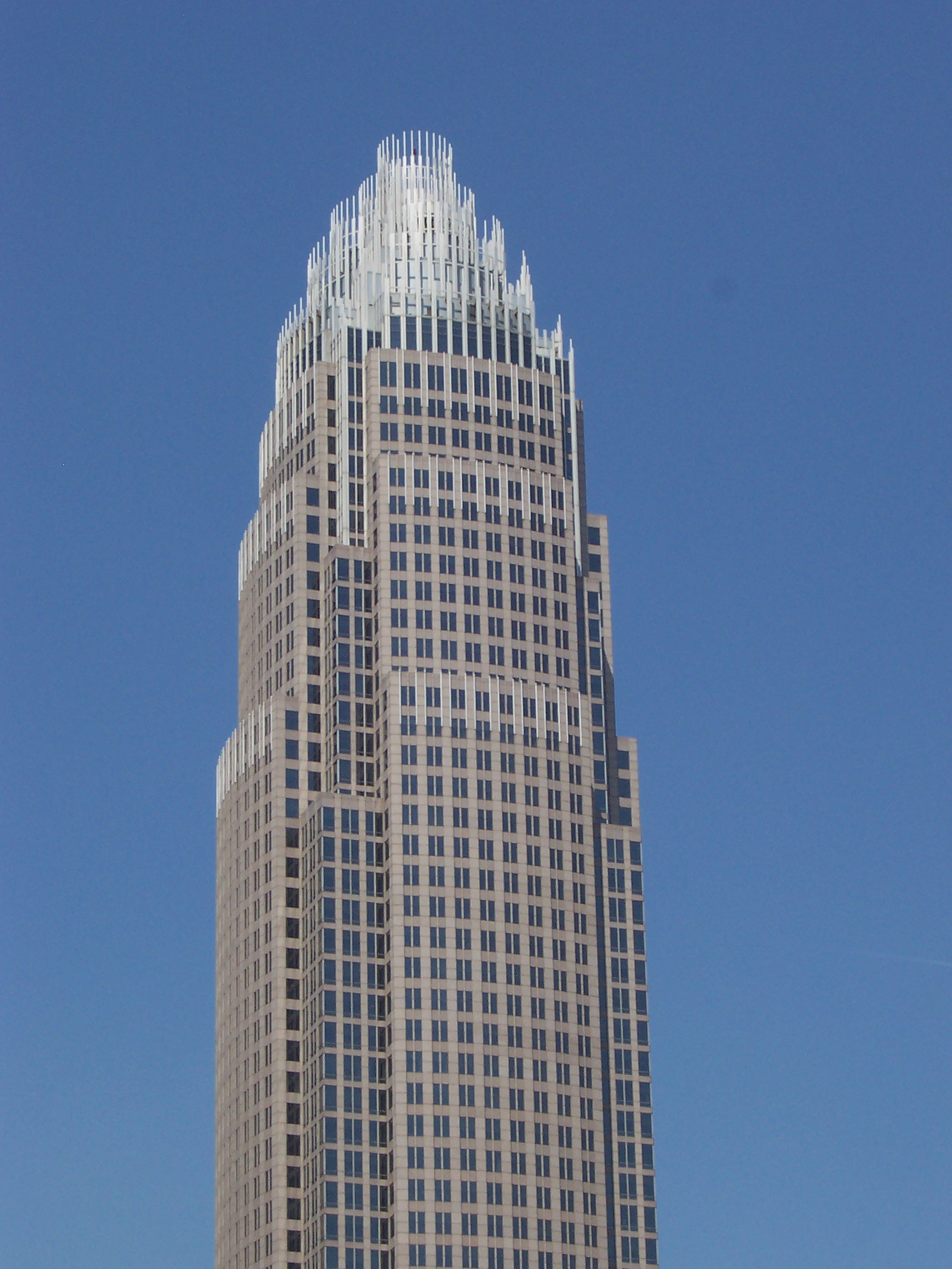 The stepped stone-and-glass crown of the Bank of America Corporate Center tower in Charlotte against clear blue sky, 2015
