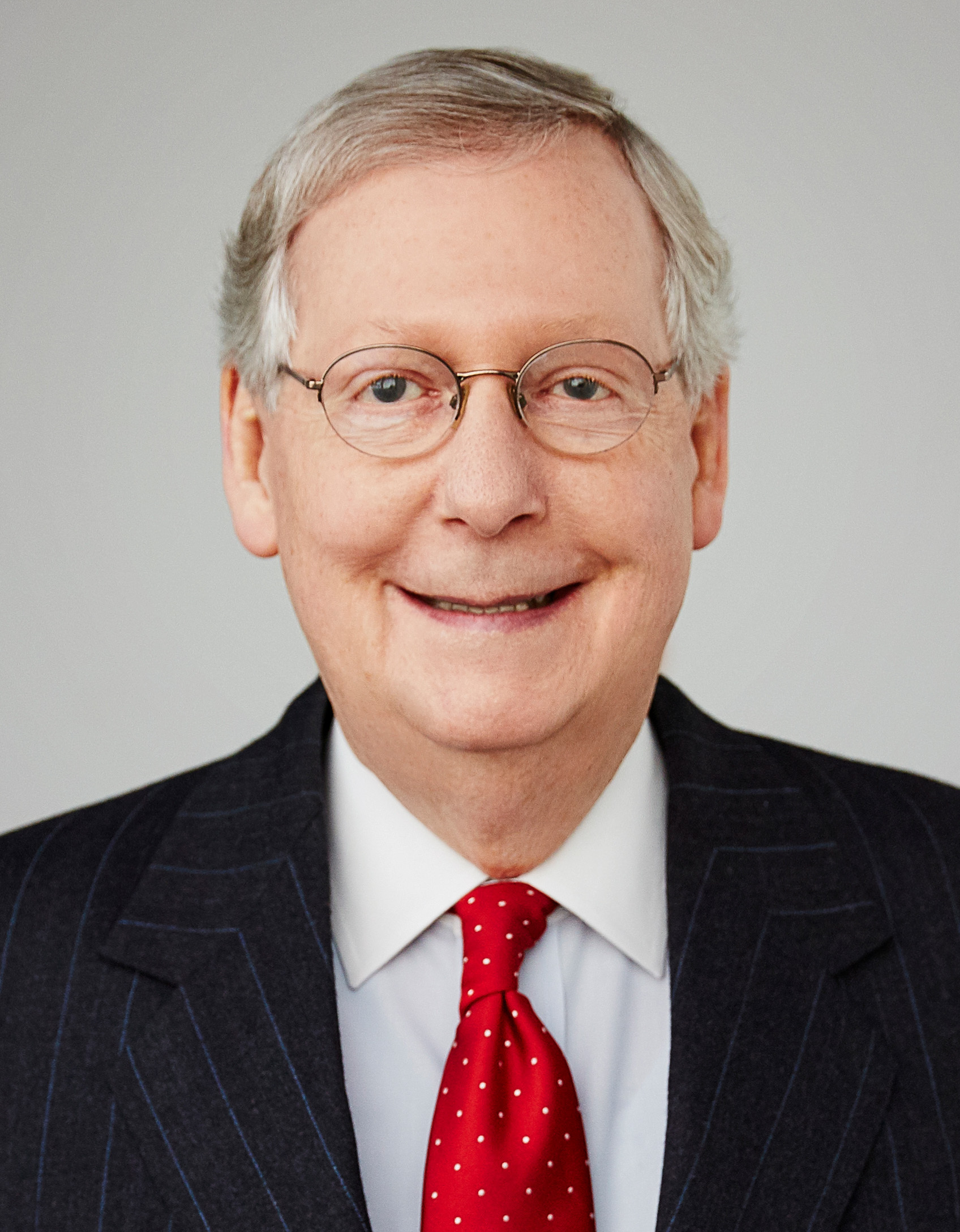 Mitch McConnell in his official Senate portrait, rimless glasses over a red polka-dot tie under a pinstripe suit, 2015
