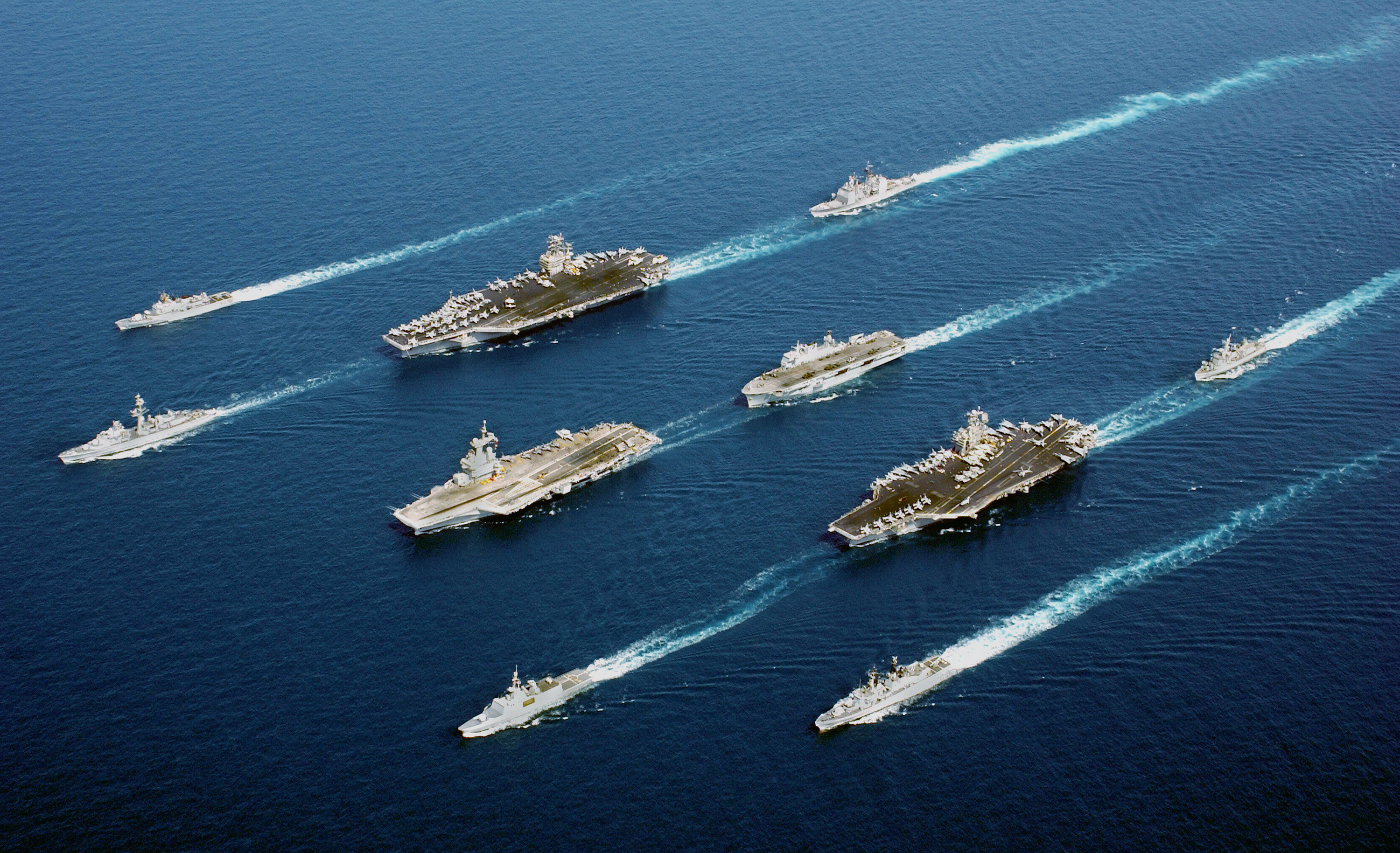 Three aircraft carriers and their escort ships steaming in wedge formation across the open sea, 2015