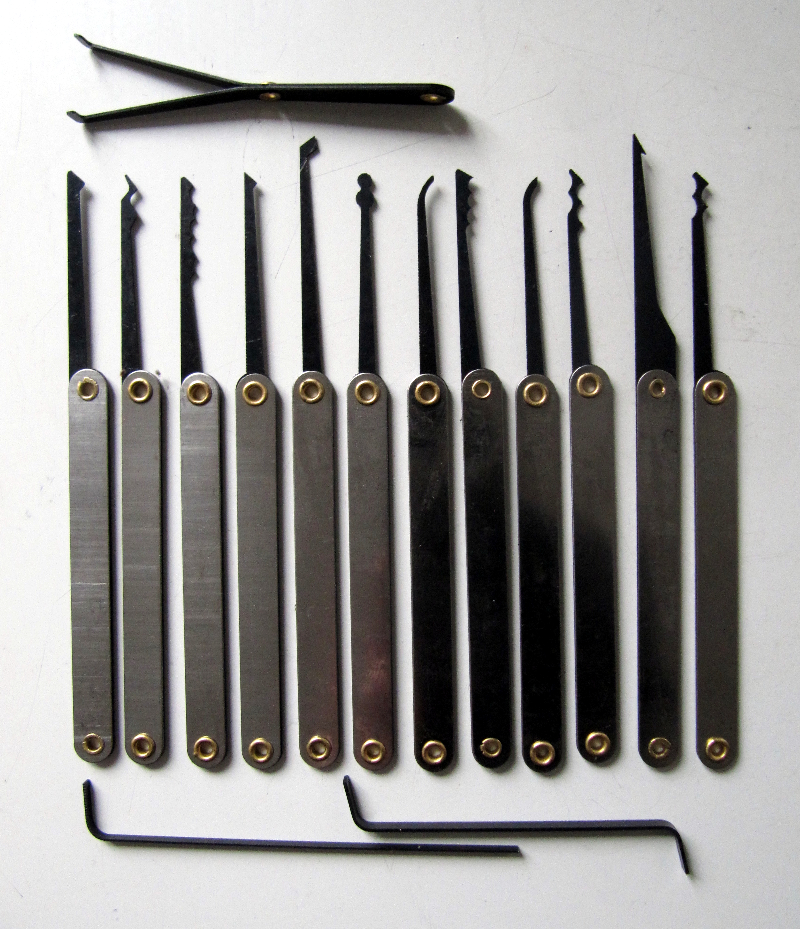 A set of black-tipped lock picks and two tension wrenches laid out in a row on a grey surface, 2015