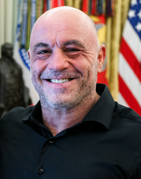 Joe Rogan in a black shirt with the US flag and military standards behind him, 2018