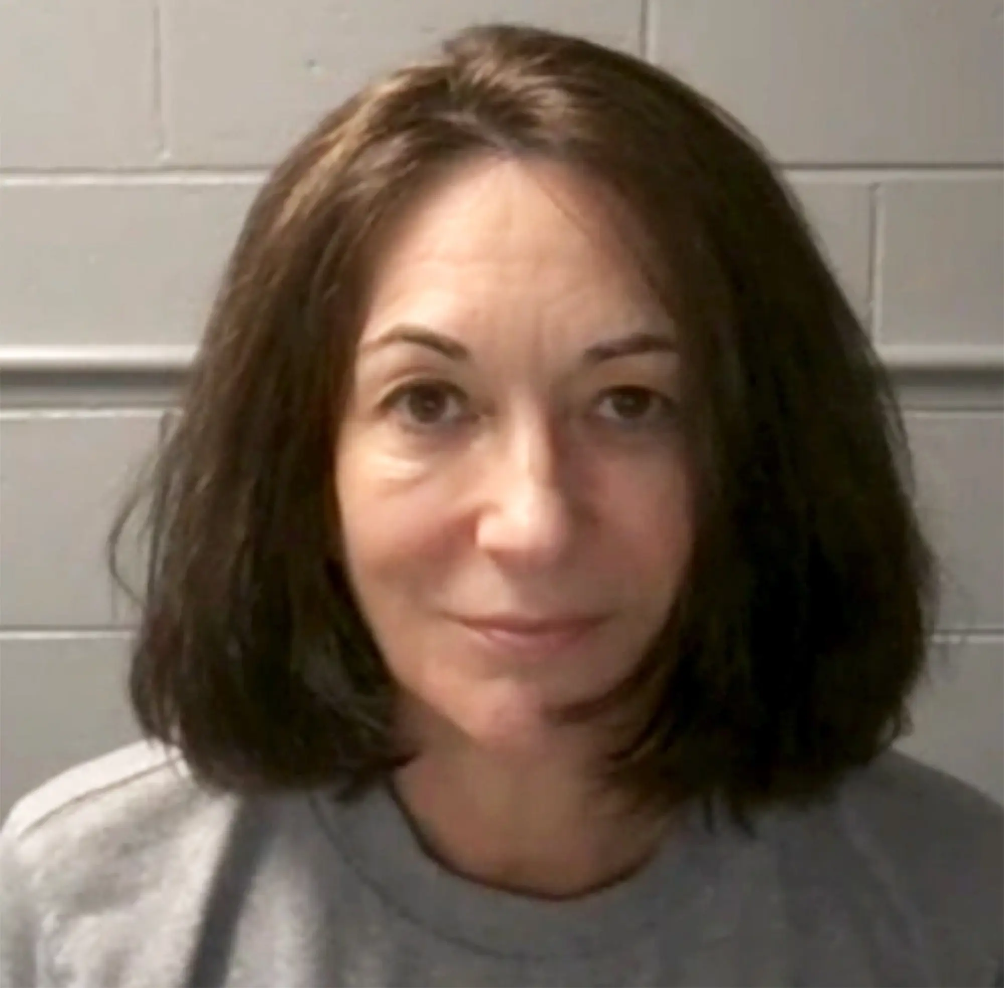 Ghislaine Maxwell in a video-frame close-up against a cinder-block prison wall, 2025