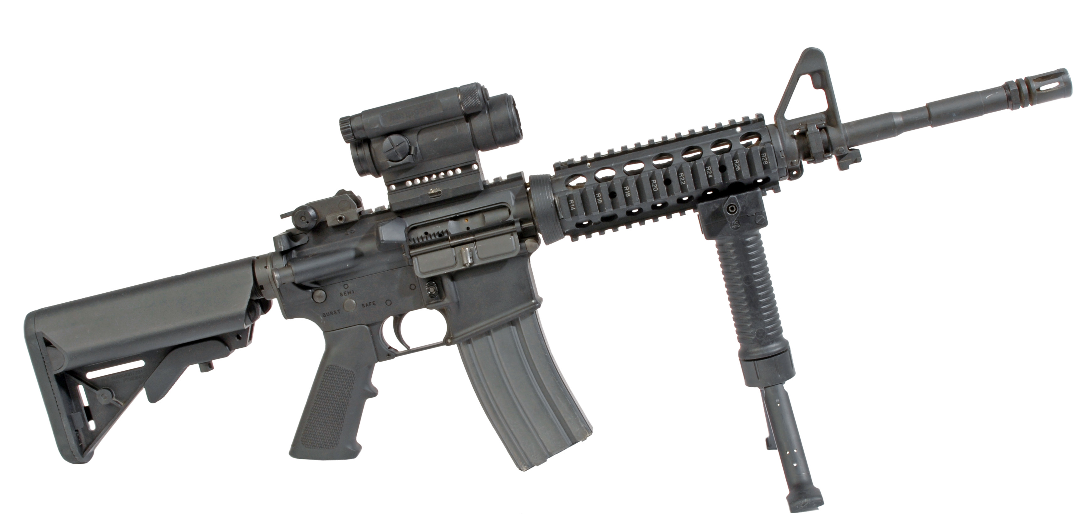 An M4A1 carbine fitted with an ACOG optic and a vertical foregrip on a bipod, photographed against a black backdrop, 2010