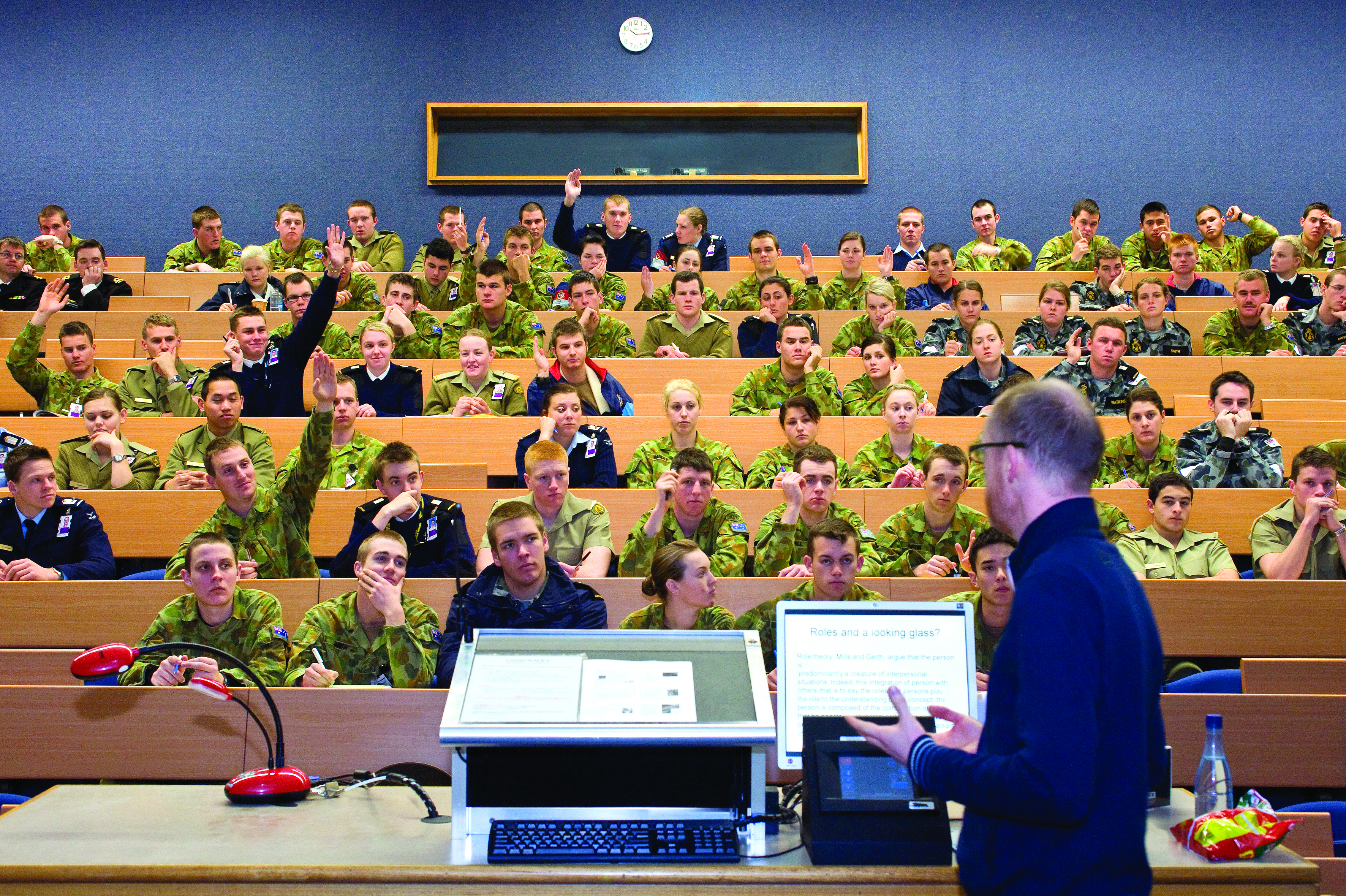 A university lecture hall of uniformed cadets in banked rows, a lecturer at the podium below the chalkboard, 2012