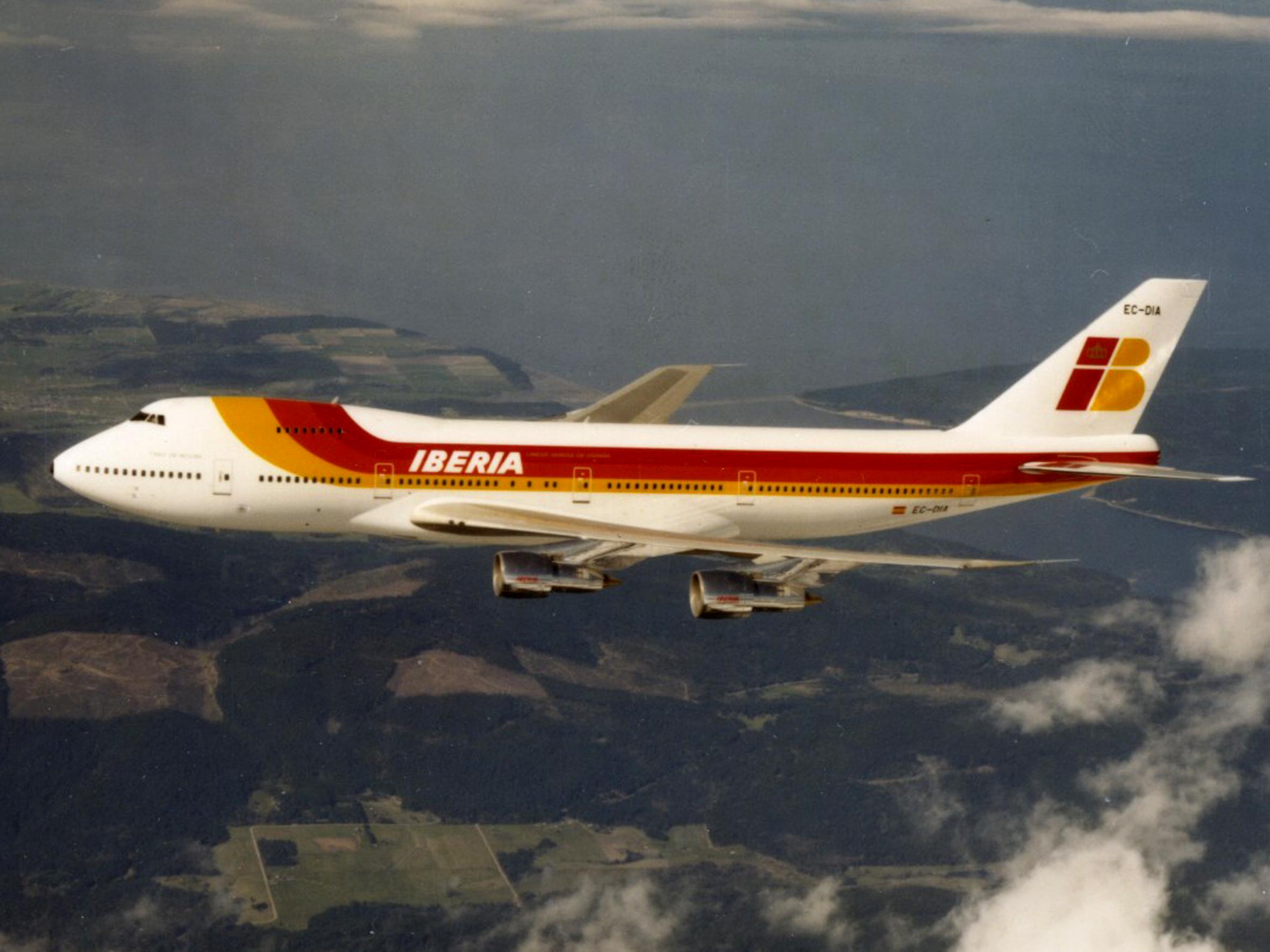 An Iberia Boeing 747 in red-and-gold livery, tail marked EC-DIA banking over a rugged coast, 1985