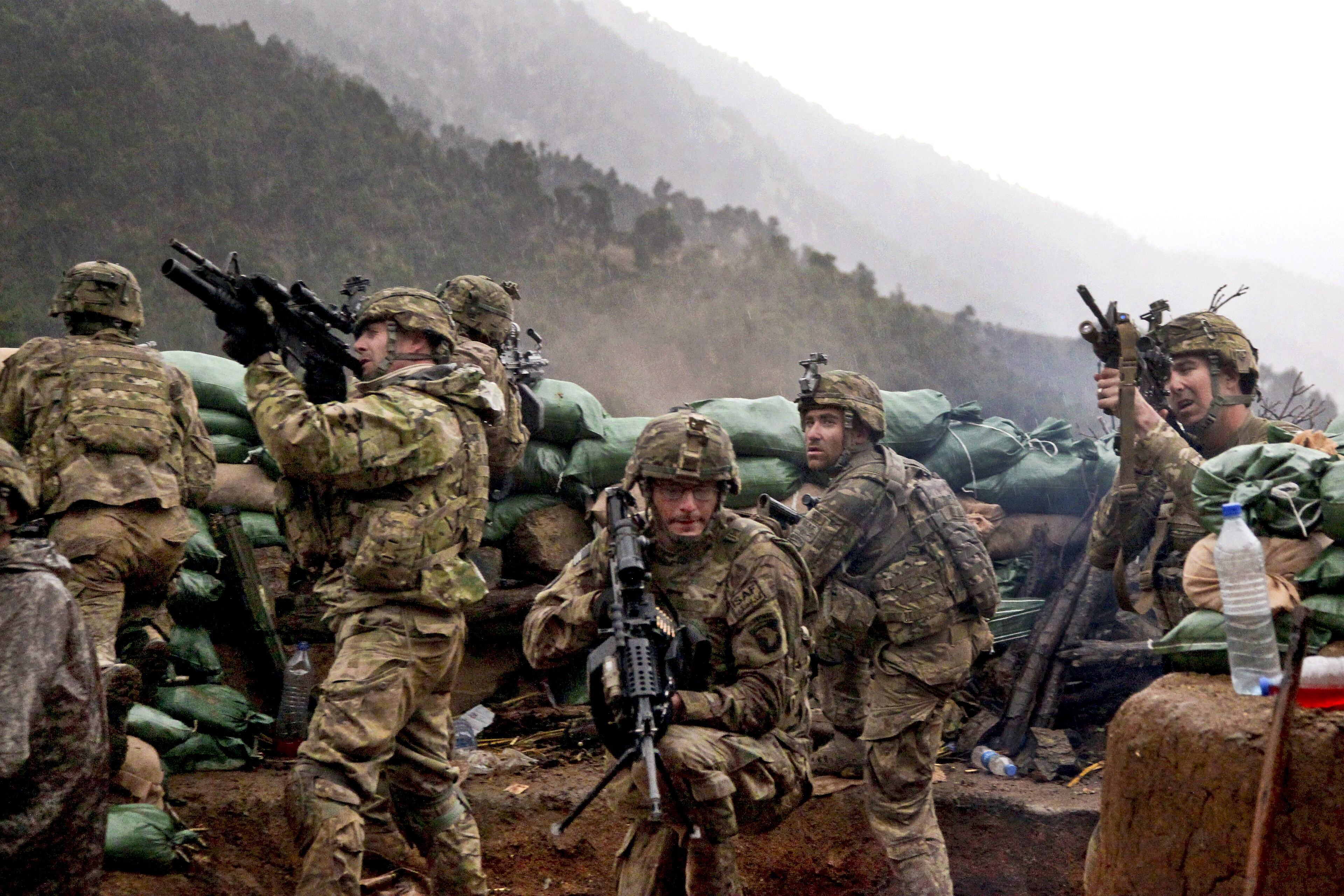 US infantry firing over a sandbag berm through rain in an Afghan mountain valley, 2011